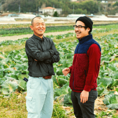 We facilitate exchanges of experiences between farmers. An older and younger Asian male laugh easily in a field of cabbages