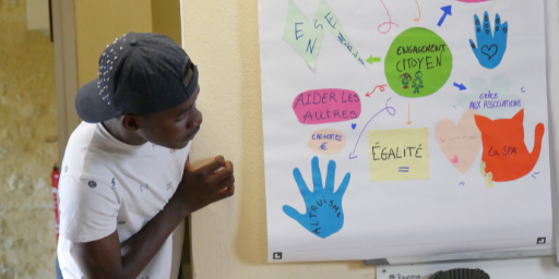 Young black male with navy baseball cap looks around wall corner at a poster with colored shapes